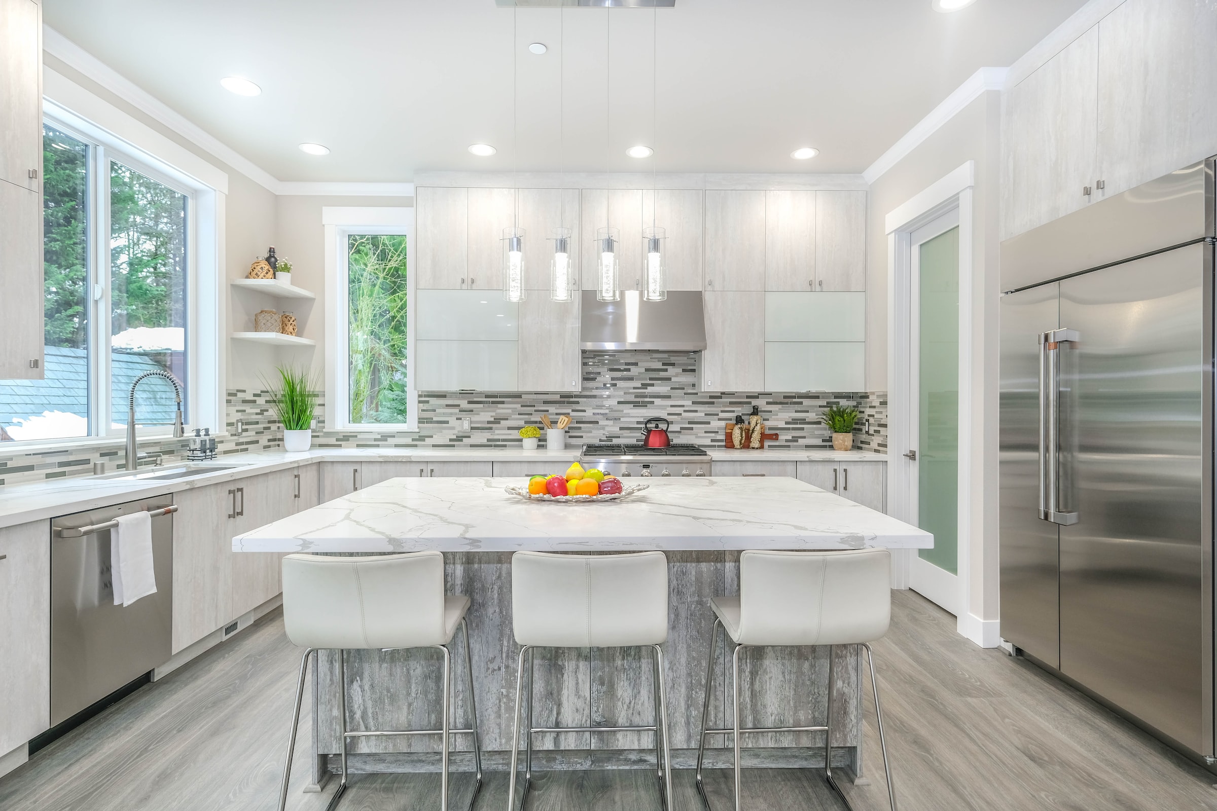 A bright modern kitchen with a white quartz island, three white bar stools and stainless steel appliances